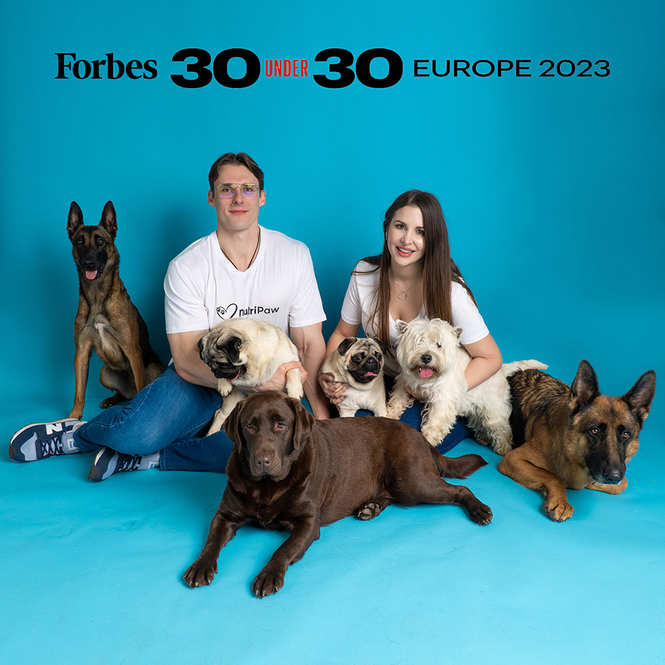 Adelina Zotta and Connor Westby posing on a blue background with five different dogs. The image has the writing 'Forbes 30 under 30 Europe 2023' at the top of the image.